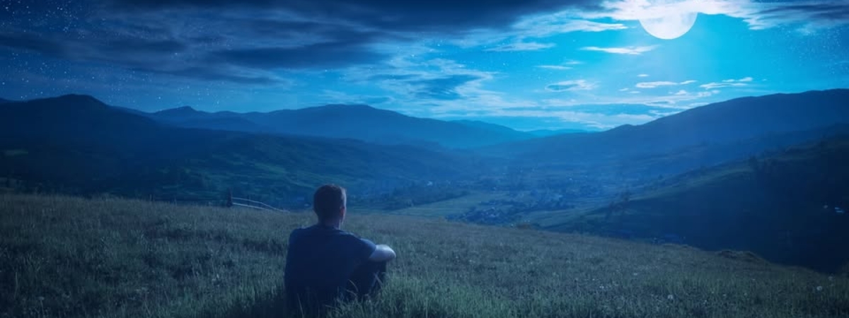 Human sitting on a hill and enjoy full moon rising in a starry sky above the night mountain valley.